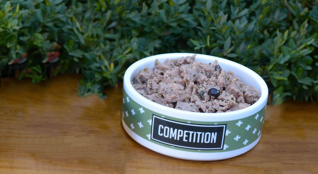 Dog bowl labeled 'Competition' filled with an unidentifiable ground mixture lacking visible whole ingredients