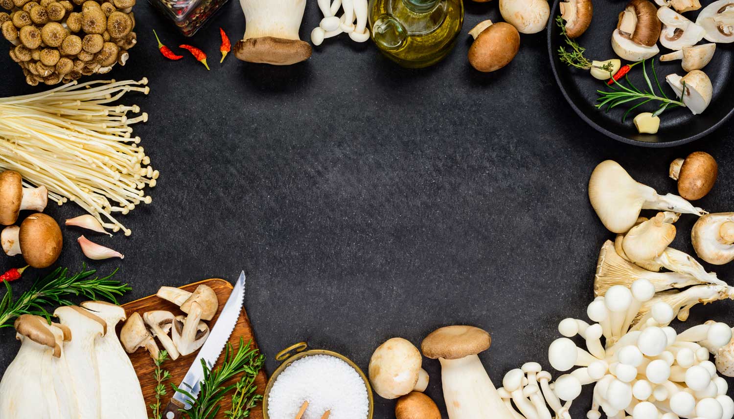 Variety of edible mushrooms on a dark background with cutting herbs and a board