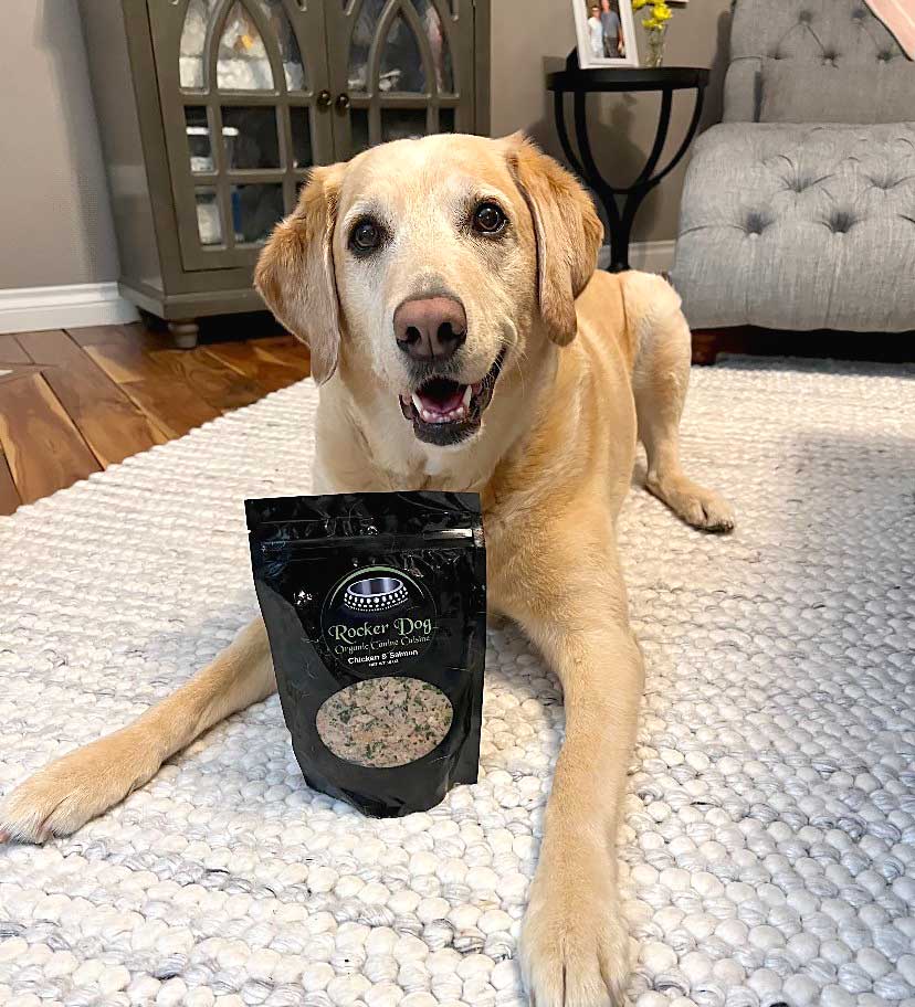 Happy yellow Labrador lying on a living-room rug with paws by a bag of Rocker Dog gently cooked fresh dog food